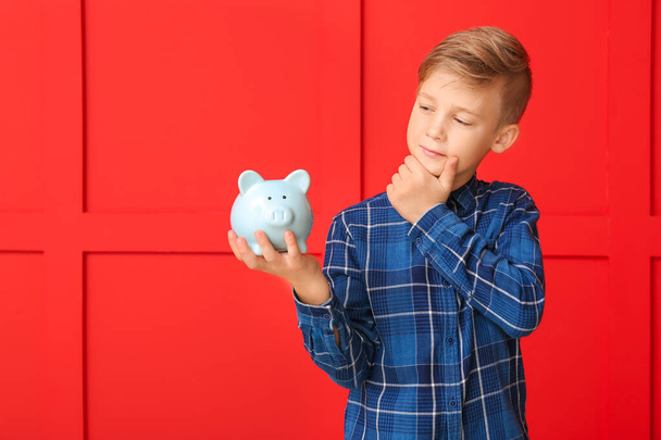 Thoughtful boy with piggy bank on color background - Photo, Image