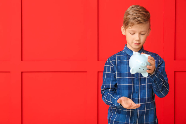 Netter Junge tippt Geld aus Sparschwein auf farbigem Hintergrund - Foto, Bild