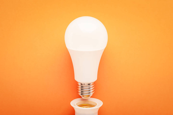 LED-Lampe aus Steckdose auf orangefarbenem Hintergrund: Energiesparkonzept und die Stunde der Erde. - Foto, Bild
