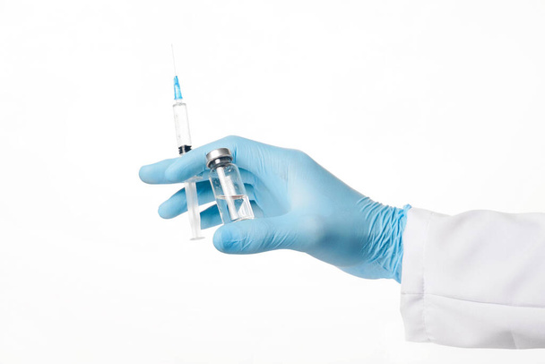 Sluit de hand van de arts in blauwe latex handschoen met glazen ampul en spuit op witte achtergrond. Gezondheid en vaccinatie - Foto, afbeelding