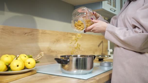 mujer cocina la cena y vierte pasta en una cacerola en la estufa
 - Imágenes, Vídeo