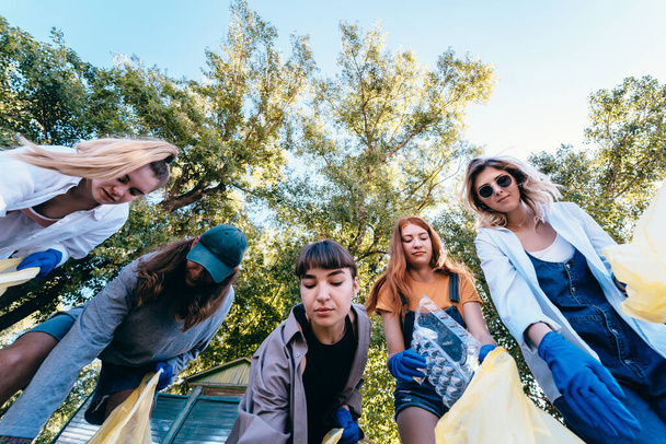 Bir grup aktivist arkadaş bir torbaya bir sürü çöp atıyor. Dibe vurma. - Fotoğraf, Görsel