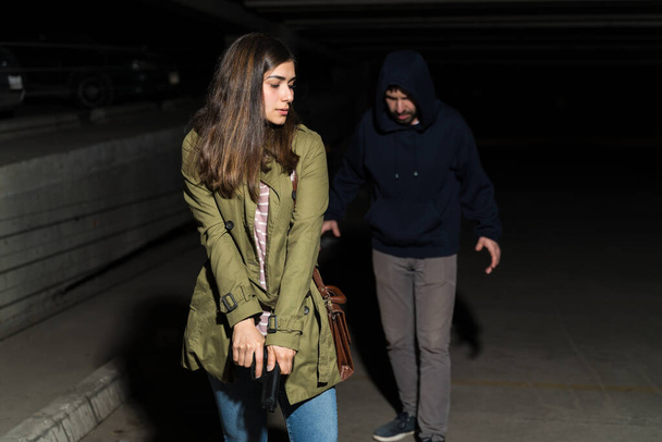 Tarkkaavainen nainen aseen kanssa kävelee rikollisen edellä pimeällä parkkipaikalla
 - Valokuva, kuva