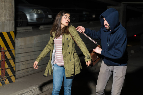 Ladrón arrebatando el bolso de la víctima sorprendida mujer caminando en el callejón oscuro por la noche
 - Foto, imagen