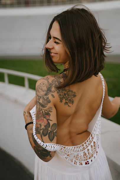 Стройная сексуальная женщина демонстрирует свою стройную спину стоя в белом платье, оглядываясь через плечо
 - Фото, изображение