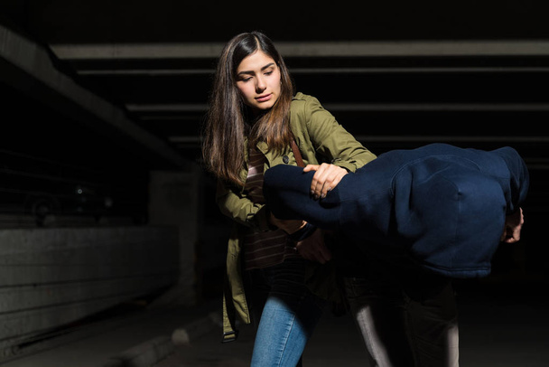 Strong confident woman fighting with bandit in dark parking lot - Photo, Image