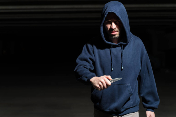 Hispánský zločinec drží nůž, zatímco stojí na tmavém parkovišti - Fotografie, Obrázek