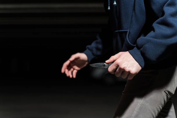 Μεσοτομή του αρσενικού ληστή που περπατάει με μαχαίρι στο σκοτάδι στο πάρκινγκ - Φωτογραφία, εικόνα