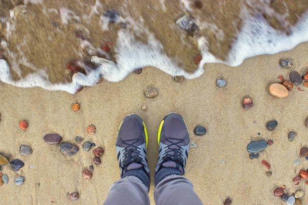 Feet in sneakers on the beach. The wave is coming - Foto, afbeelding