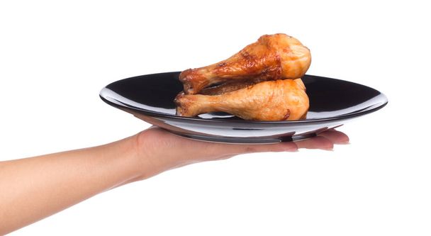 χέρι κρατώντας ψημένο πόδι κοτόπουλου σε ένα πιάτο που απομονώνεται σε λευκό φόντο - Φωτογραφία, εικόνα
