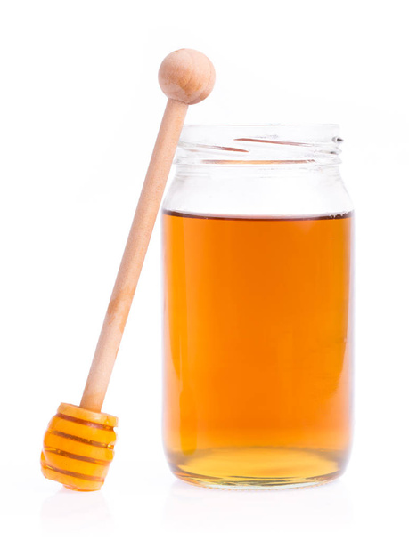 Glass bottle full of honey and wooden stick on a white background. - Фото, зображення