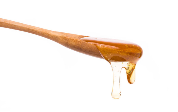 Honey dripping from a spoon wooden isolated on white background - Fotografie, Obrázek