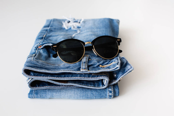 Jeans and sunglasses neatly folded on a white background  - Foto, imagen