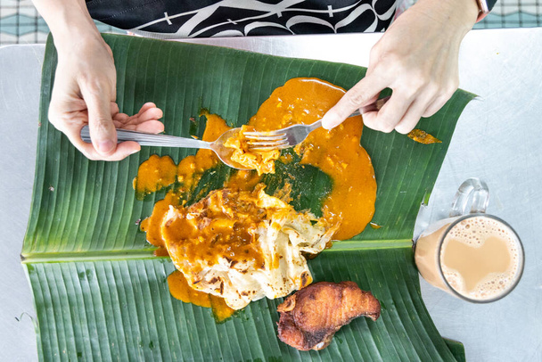 Vue aérienne de la personne qui mange du roti canai ou du paratha avec curry sur feuille de banane avec thé ou thé au lait, petit déjeuner malaisien préféré
 - Photo, image