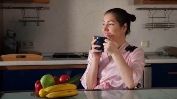 kobieta siedzi przy stole i wącha zapach kawy trzymając filiżankę - Materiał filmowy, wideo