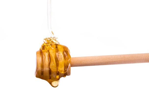 Honey dripping from a wooden honey dipper isolated on white background - Fotoğraf, Görsel