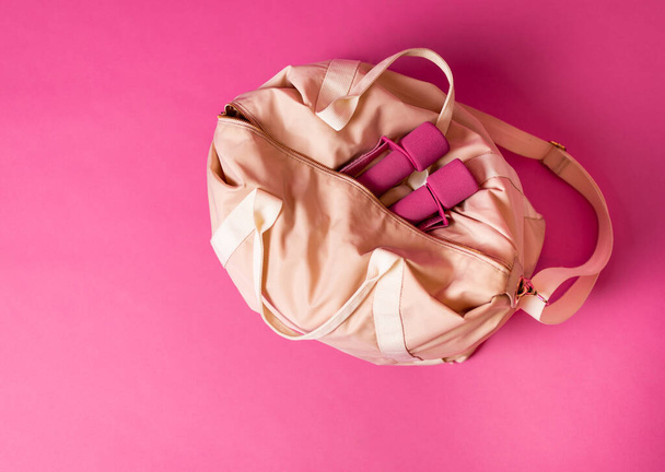 Women sports bag with dumbbells lying on pink background - Foto, Imagen