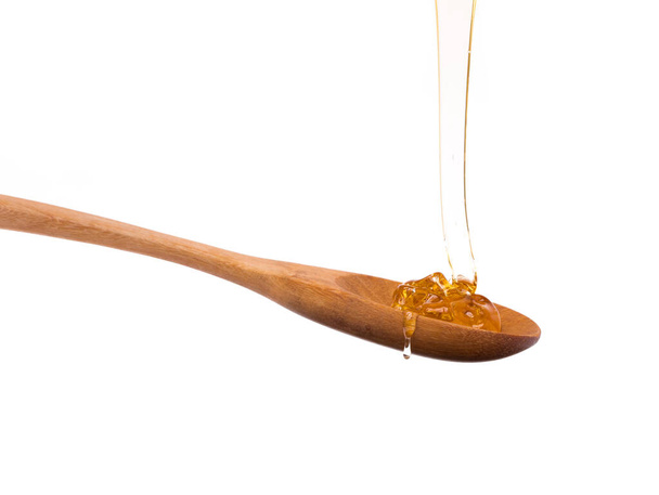 Honing druipend van een lepel hout geïsoleerd op witte achtergrond - Foto, afbeelding