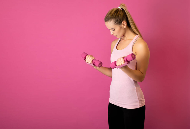 Attractive fitness woman holding dumbells on pink background - Photo, image
