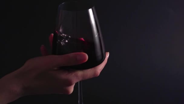 A wine expert rotates and tests a glass of drink at a winery. The final process of making alcohol. Isolated, static shot, black background - Imágenes, Vídeo