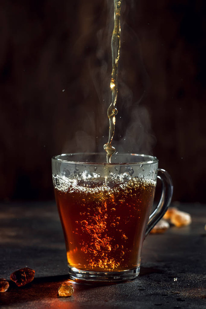Black tea pouring into glass cup with natural steam on brown background - Valokuva, kuva