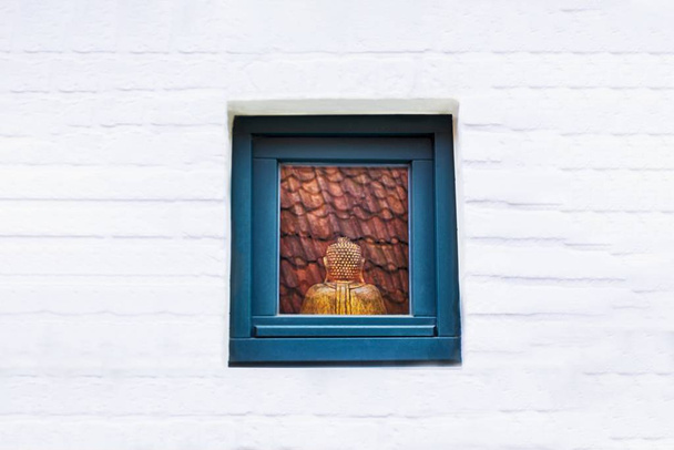 Άγαλμα του Βούδα στο παράθυρο. Χάλκινος Βούδας κάθεται πίσω. Λευκός τοίχος, αντίγραφο χώρου - Φωτογραφία, εικόνα