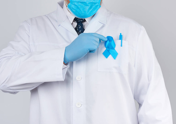 male doctor in a white coat and tie stands. On the pocket pinned a blue ribbon in the shape of a loop, symbol of the fight and treatment of prostate cancer - Foto, immagini