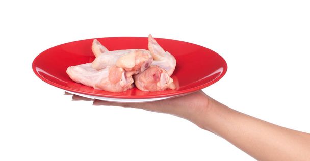 mano sosteniendo Raw Chicken wings meaton un plato aislado sobre fondo blanco
 - Foto, imagen
