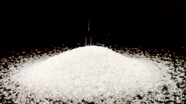 Small pieces of sugar are poured on the sugar mountain. The concept of sweet tooth. Macro video granules of sugar on a black background. - Footage, Video