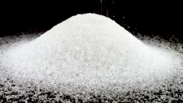 Kleine stukjes suiker worden op de suikerberg gegoten. Het concept van zoetekauw. Macro video granulaat van suiker op een zwarte achtergrond. - Video