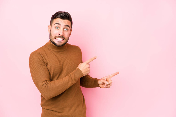 Young caucasian man against a pink background isolated shocked pointing with index fingers to a copy space. - Фото, зображення