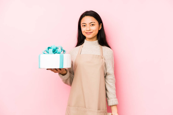 Nuori kiinalainen nainen tilalla kakku eristetty henkilö osoittaa käsin paita kopioi tilaa, ylpeä ja luottavainen
 - Valokuva, kuva