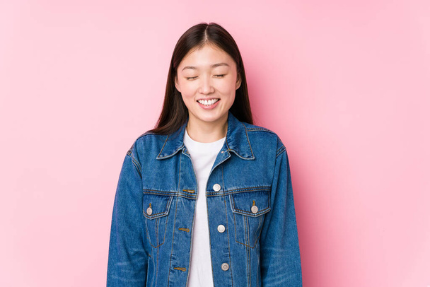 Young chinese woman posing in a pink background isolated laughs and closes eyes, feels relaxed and happy. - Фото, изображение