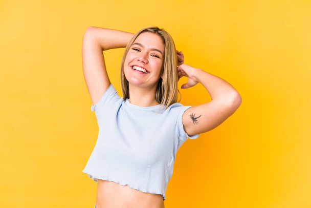 Young blonde caucasian woman isolated on yellow background stretching arms, relaxed position. - 写真・画像