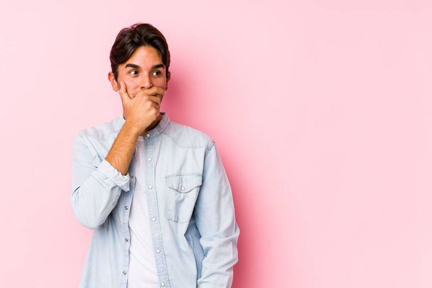 Young caucasian man posing in a pink background isolated thoughtful looking to a copy space covering mouth with hand. - Foto, immagini
