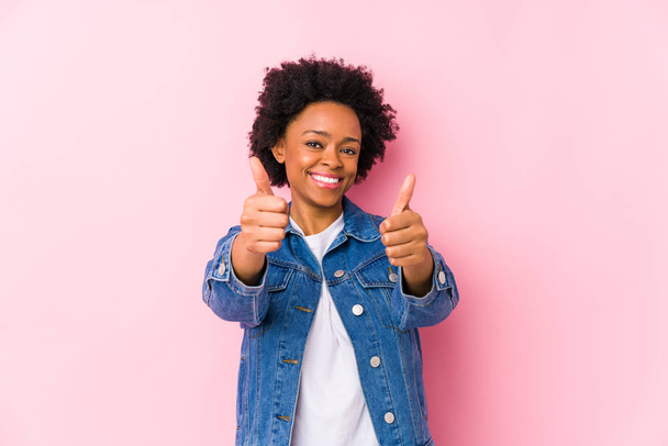 Jovem afro-americana contra um pano de fundo rosa isolado com polegares para cima, aplausos sobre algo, apoio e respeito conceito
. - Foto, Imagem