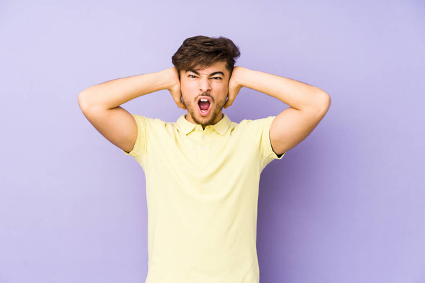 Young arabian man isolated on a purple background covering ears with hands trying not to hear too loud sound. - Foto, Imagen
