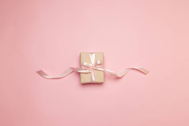 Minimale Urlaubs-Komposition aus Geschenkschachtel mit rosa Seidenschleife auf rosa Hintergrund. Grußkarte oder Einladungsvorlage. - Foto, Bild