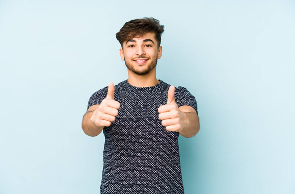 Young arabian man isolated on a blue background with thumbs ups, cheers about something, support and respect concept. - Photo, Image