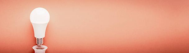 Λαμπτήρας Led ανεστραμμένος από ένα φυσίγγιο σε κόκκινο φόντο με αντιγραφή space web banner: έννοια της τεχνολογίας εξοικονόμησης ενέργειας και Earth Hour. - Φωτογραφία, εικόνα