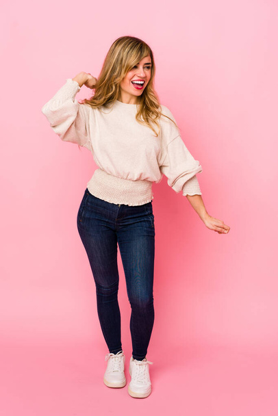 Young blonde caucasian woman standing over a pink background dancing and having fun. - Foto, Imagen