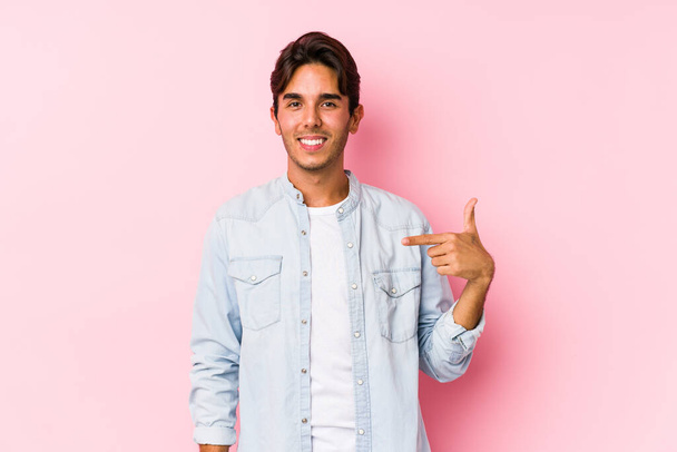 Young caucasian man posing in a pink background isolated person pointing by hand to a shirt copy space, proud and confident - Foto, imagen