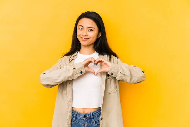 Mladá Číňanka izolované na žlutém pozadí s úsměvem a ukazující tvar srdce s rukama. - Fotografie, Obrázek