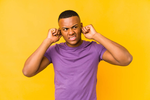 Young latin man isolated on yellow background covering ears with hands. - Photo, Image