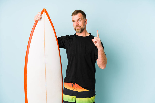 Surfen άνθρωπος απομονώνονται σε μπλε φόντο δείχνει νούμερο ένα με το δάχτυλο. - Φωτογραφία, εικόνα