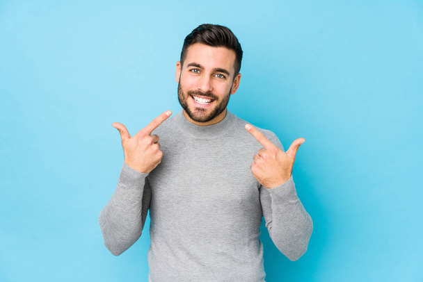 Junger kaukasischer Mann vor blauem Hintergrund lächelt vereinzelt und zeigt mit dem Finger auf den Mund. - Foto, Bild