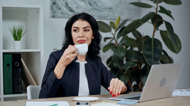 mulher de negócios atraente digitando no laptop e sorrindo enquanto bebe café
 - Filmagem, Vídeo