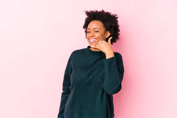 Middle aged african american woman against a pink background isolated showing a mobile phone call gesture with fingers. - Photo, image