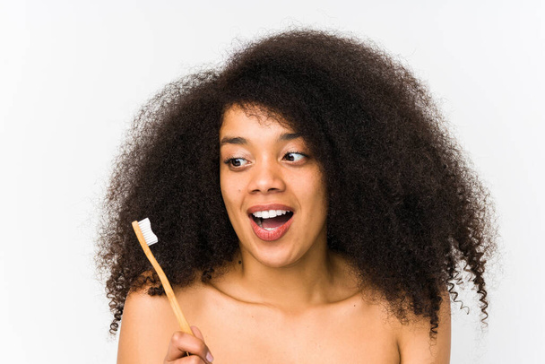 Молодая афро-женщина, держащая зубную щетку, впечатлена, удерживая пространство для копирования на ладони
. - Фото, изображение
