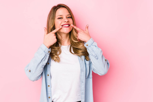Young caucasian woman isolated on pink background smiles, pointing fingers at mouth. - Foto, Bild